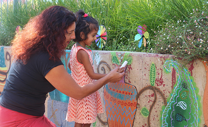 Teffany helping a small child to make her mark on a Tuggeranong wall to celebrate multiculturalism